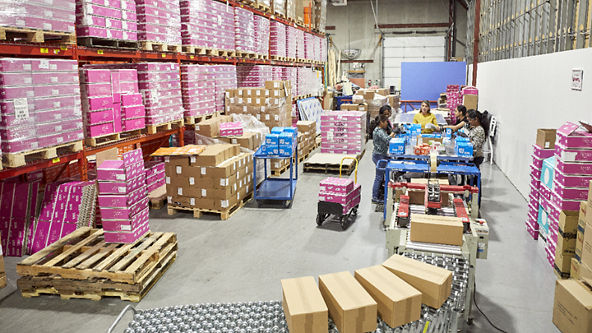 Group of women packing orders with boxes on a metal conveyor belt
