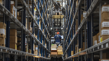 Two forklifts stacked on top each other going between shelves of boxes