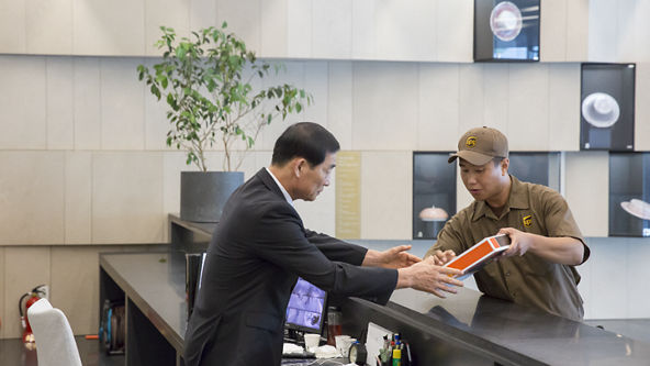 Male UPS driver handing a package to a male at a buildings front desk