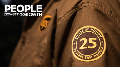 Close-up of a brown uniform sleeve featuring a circular embroidered patch. The patch prominently displays the number 25 in the center with the words CIRCLE OF HONOR and 25 YEARS SAFE DRIVING around the edge. A shield-shaped badge is also visible on the chest area of the uniform. Warm lighting emphasizes the texture of the fabric and stitching, creating a sense of achievement and recognition.