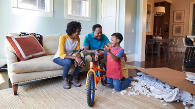 Male and female giving a new orange bike to their son 