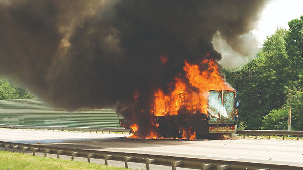 Semi-truck on fire with dark smoke on the side of the road