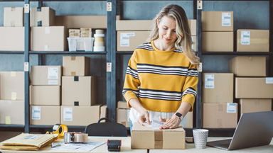 Female placing shipping label on package in front of shelves of boxes 