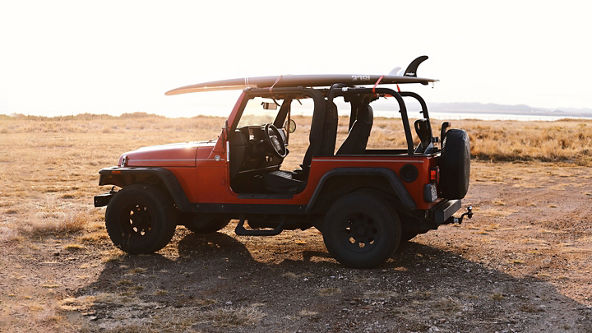 Red Jeep without doors parked on beach with surfboard attached to roof