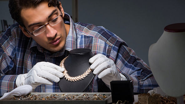 Male jeweler wearing white gloves working on a gold and diamond necklace