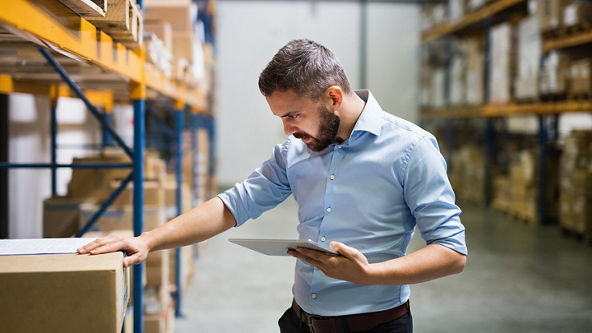 Male checking a box and holding a tablet in a warehouse