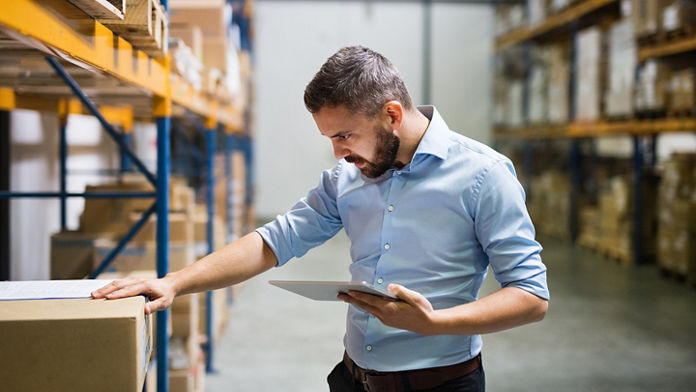 Male checking a box and holding a tablet in a warehouse