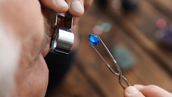 Male jeweler looking through a magnifying tool at a blue gemstone