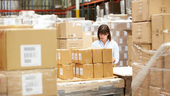 Female checking a box while surrounded by multiple boxes in a warehouse 