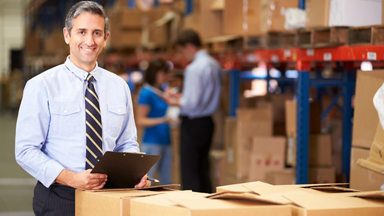 Male standing over pallet of goods with clipboard in warehouse setting
