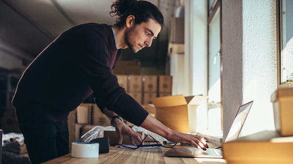 Male using a laptop for orders while surrounded by shipping supplies