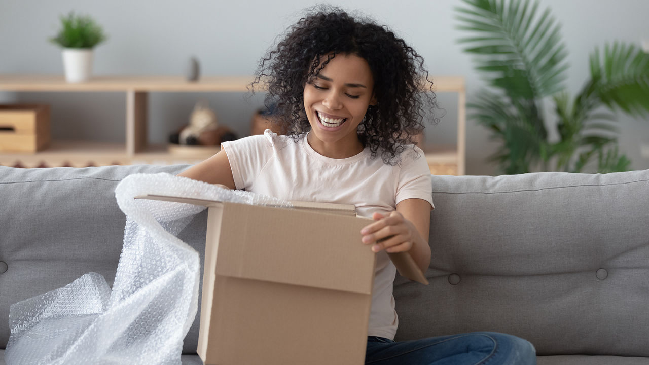 Woman sitting on the couch, opening a box. 