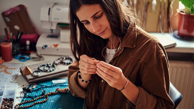 Female hand making beaded jewelry at home 
