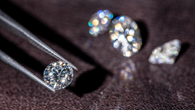 Diamonds on dark background with tweezer holding one round diamond
