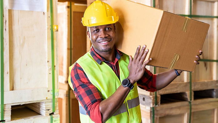 Male in hard hat and vest carrying box over his shoulder in warehouse