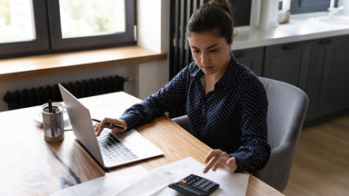 Bookkeeping. Busy millennial indian woman professional accountant preparing annual financial report checking result on calculator. Mixed race female freelancer counting tax rates declaring income; Shutterstock ID 1868366599;