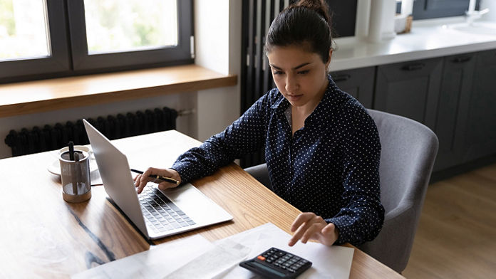 Female using a calculator and a laptop at a desk 
