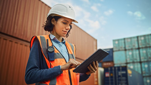 Female wearing a hard hat and a safety vest using a tablet at a loading dock
