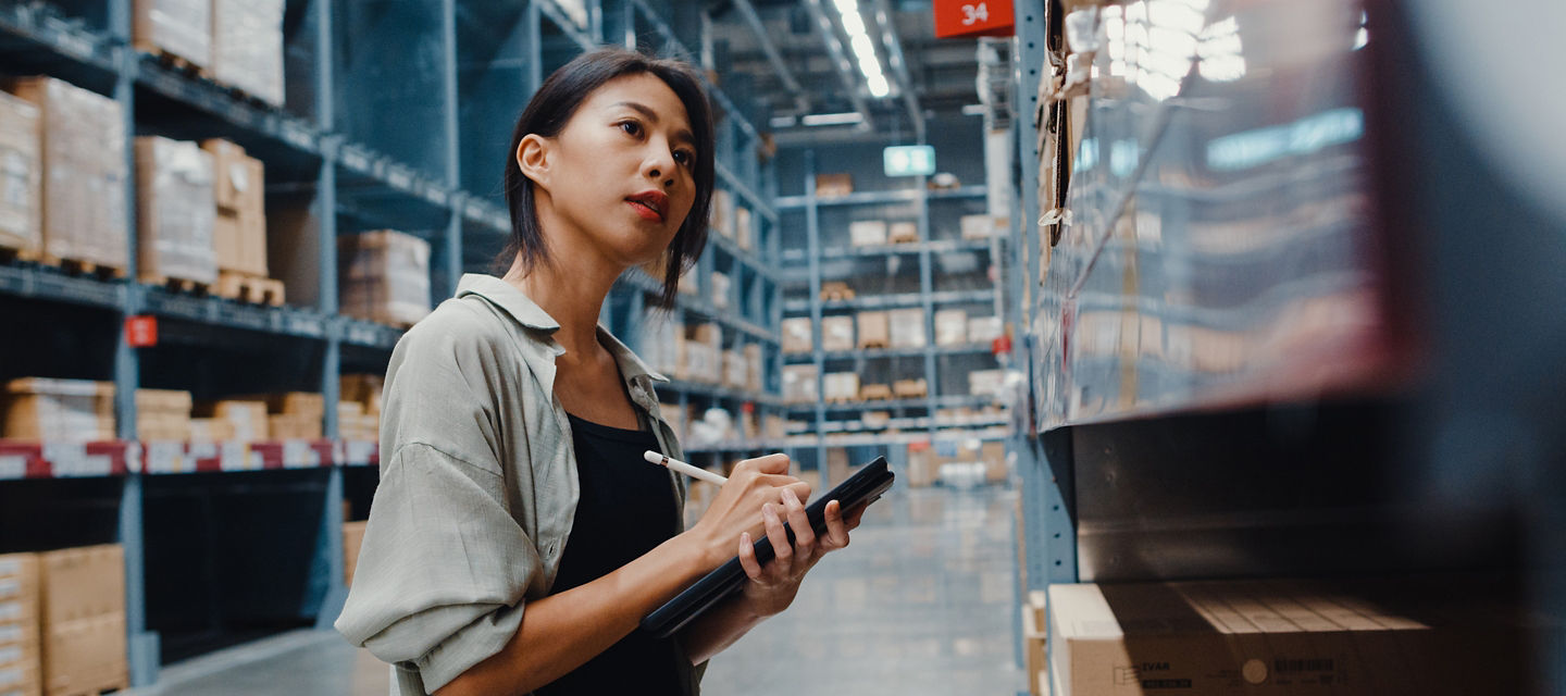 Female in a warehouse looking at an item on a shelf making a note in a tablet