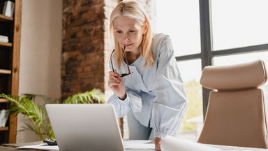 Female holding her glasses and leaning down to look at her laptop
