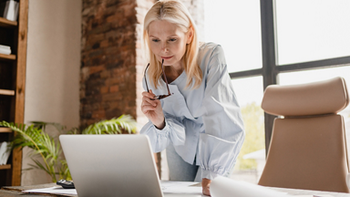 Woman holding glasses in one hand standing over laptop