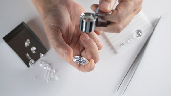 Hands using a magnifying tool to inspect a large diamond 
