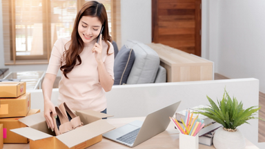 Female placing a pair of women's loafers in a box while holding her phone
