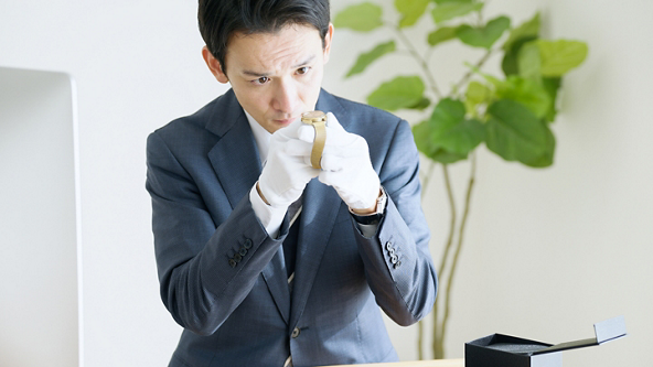 Male jeweler wearing white gloves and inspecting a gold watch 
