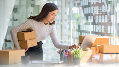 Woman with boxes under her arm working on lap top
