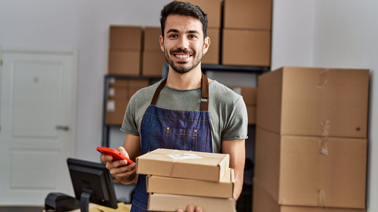Male in an apron holding three boxes and his cell phone