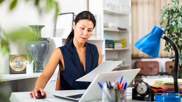 Female looking at paper while using her laptop in a home office