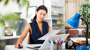 Female holding a paper and using a laptop 