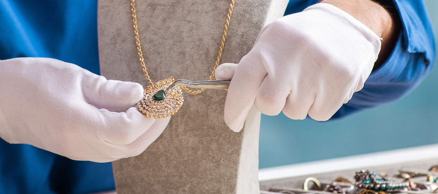 Person in white gloves using a tweezer to work on a necklace
