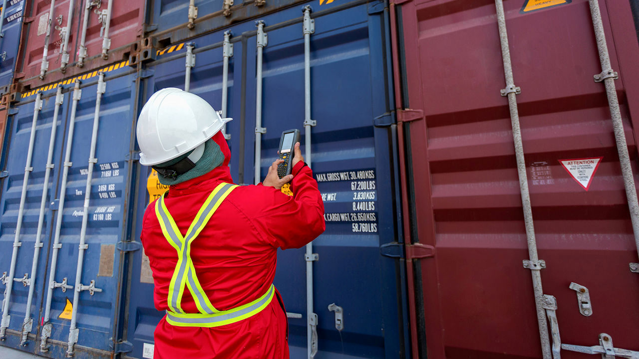 Male wearing safety gear entering a shipping containers information into a device