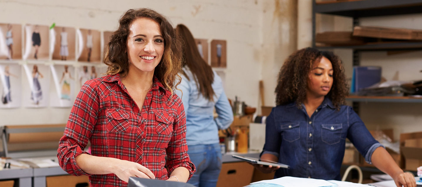 Three women in a warehouse packing item in plastic bag